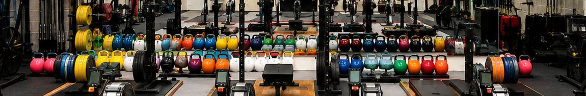 A long row of colour-coded kettlebells beside racked bumper plates