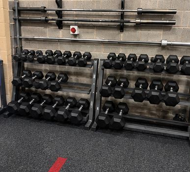 A barbell storage rack beside racked dumbbells against the wall