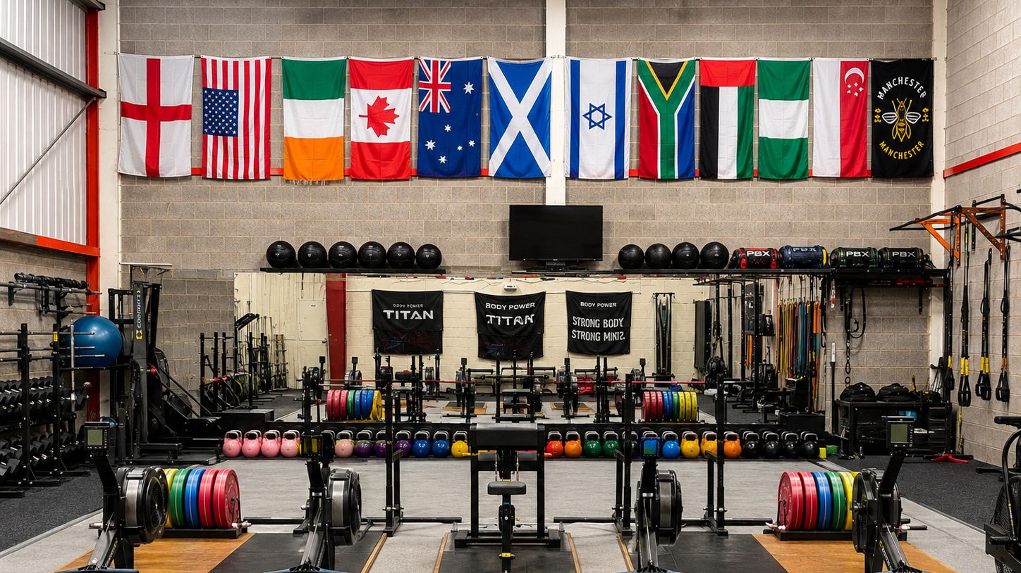 The Physical Performance training floor, with lifting platforms, racked plates and rowing machines beneath a wall of international flags