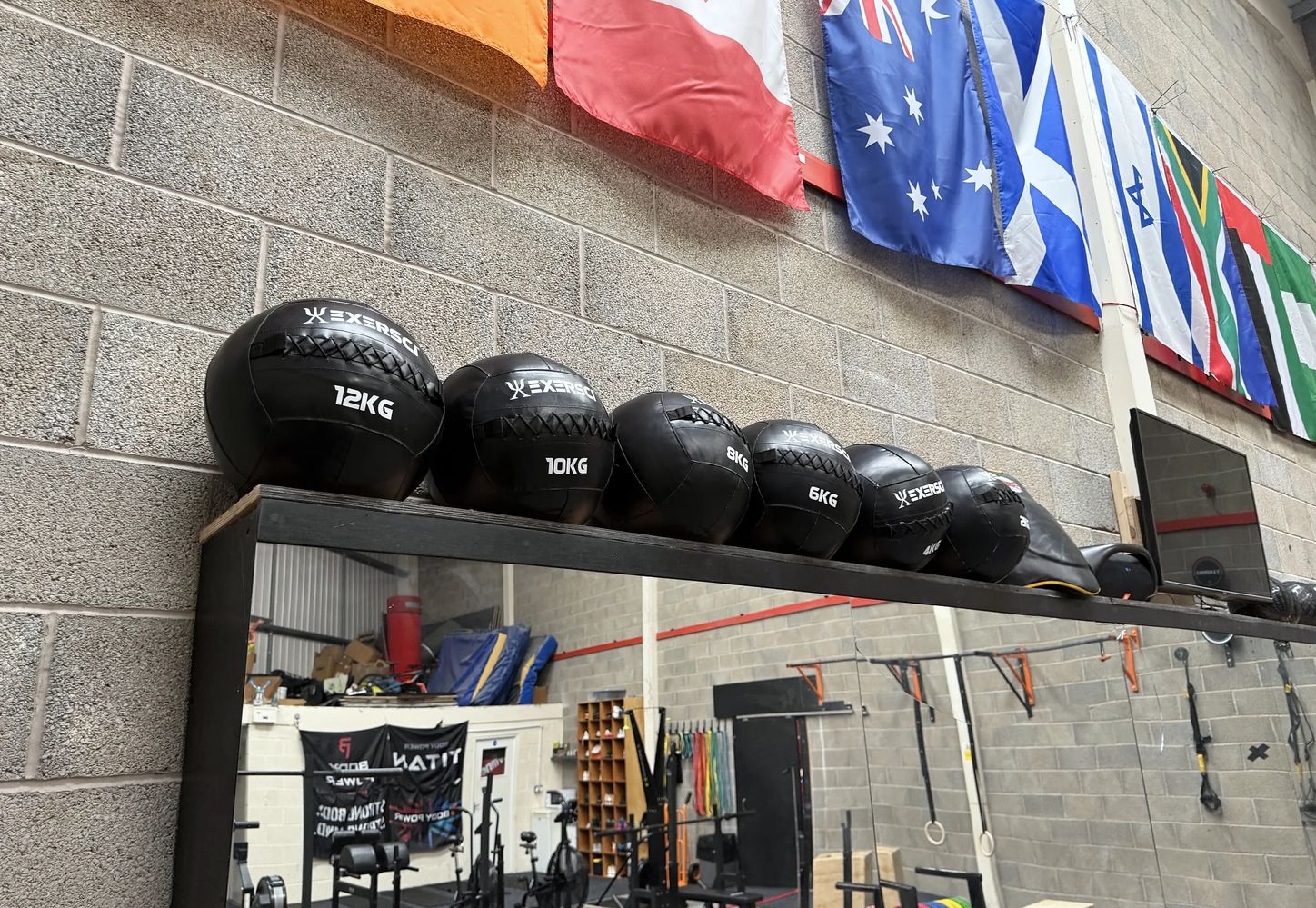 Wall mirror above a shelf of weighted balls, with the flag wall reflected behind