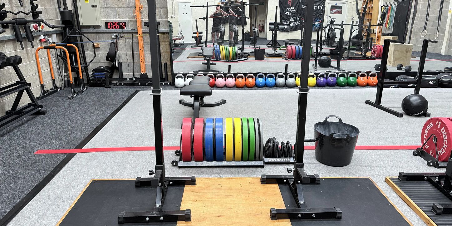 The main rig with colour-coded bumper plates, dumbbells and accessories along the wall