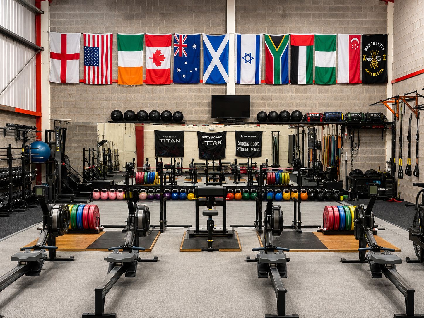 The Physical Performance training floor, with lifting platforms, racked plates and rowing machines beneath a wall of international flags