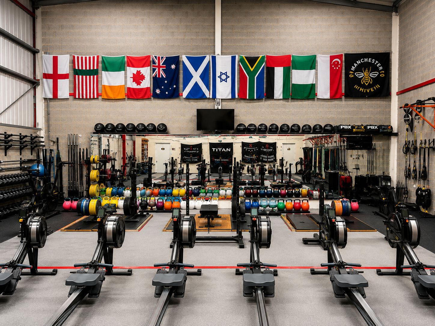 Wide view of the training floor: rowing machines, a long row of kettlebells, racked plates and lifting platforms